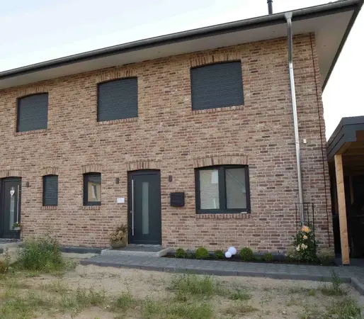 Modernes Reihenhaus mit Klinkerfassade, dunklen Fenstern und gepflegtem Vorgarten.