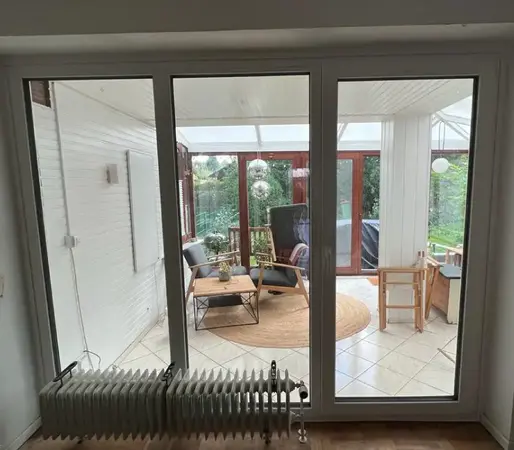 Moderner Wintergarten mit großen Fenstern, gemütlicher Sitzecke und Gartenblick.