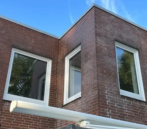Eckiges Klinkerhaus mit weißen Kunststofffenstern und Markise vor blauem Himmel.