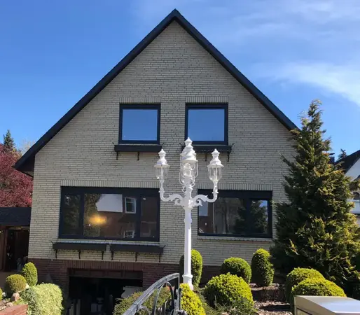 Einfamilienhaus mit gepflegtem Vorgarten, moderner Straßenlaterne und blauer Himmel.