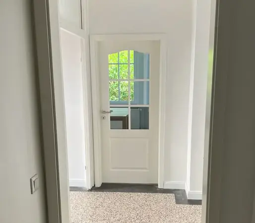 Heller Flur mit weißer Innentür, Glaseinsatz und Blick auf grünen Garten im Hintergrund.